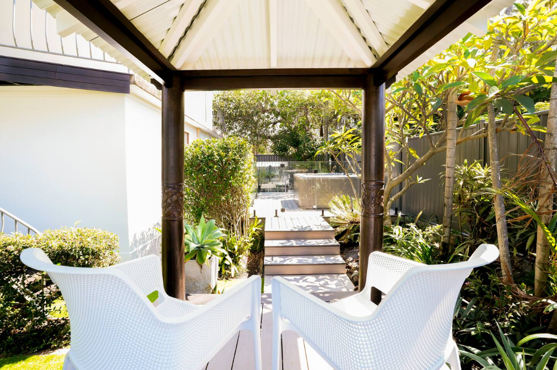 Two white chairs are sitting under a gazebo in a garden.
