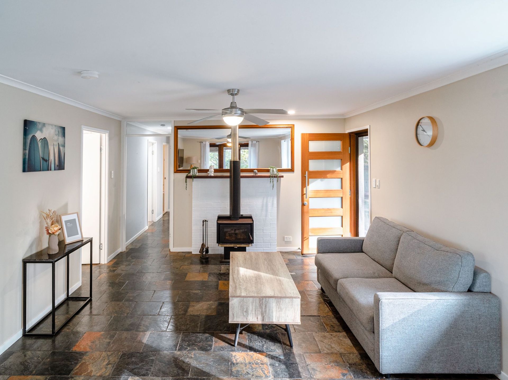 A living room with a couch , coffee table , fireplace and ceiling fan.