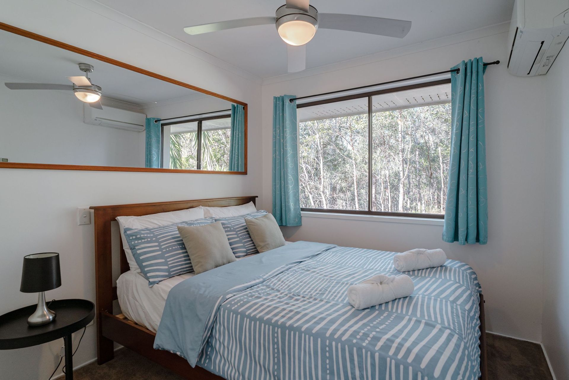 A bedroom with a king size bed , a mirror , a ceiling fan , and blue curtains.