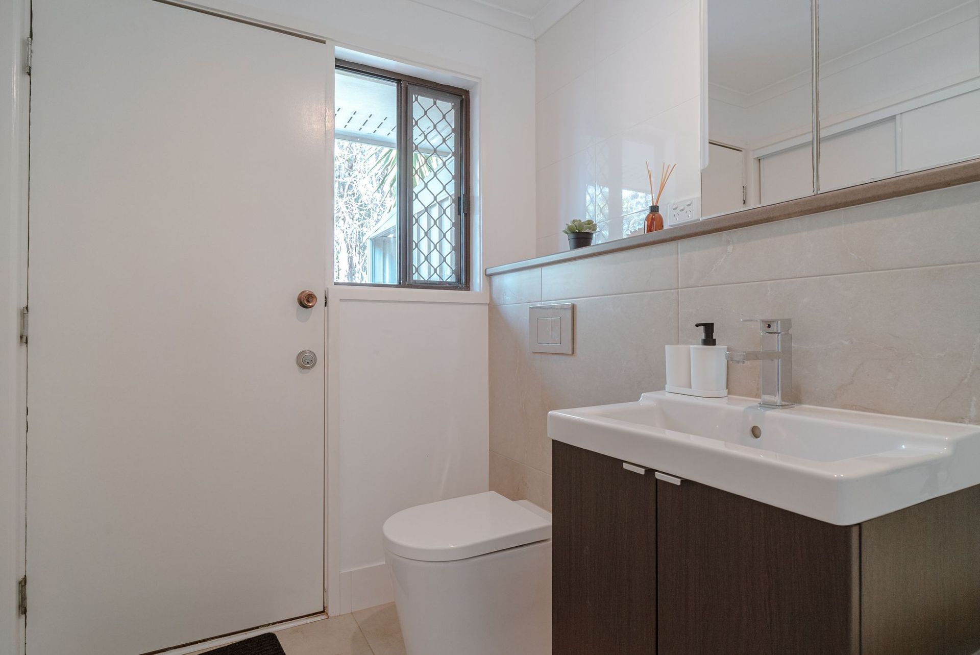 A bathroom with a toilet , sink , mirror and window.