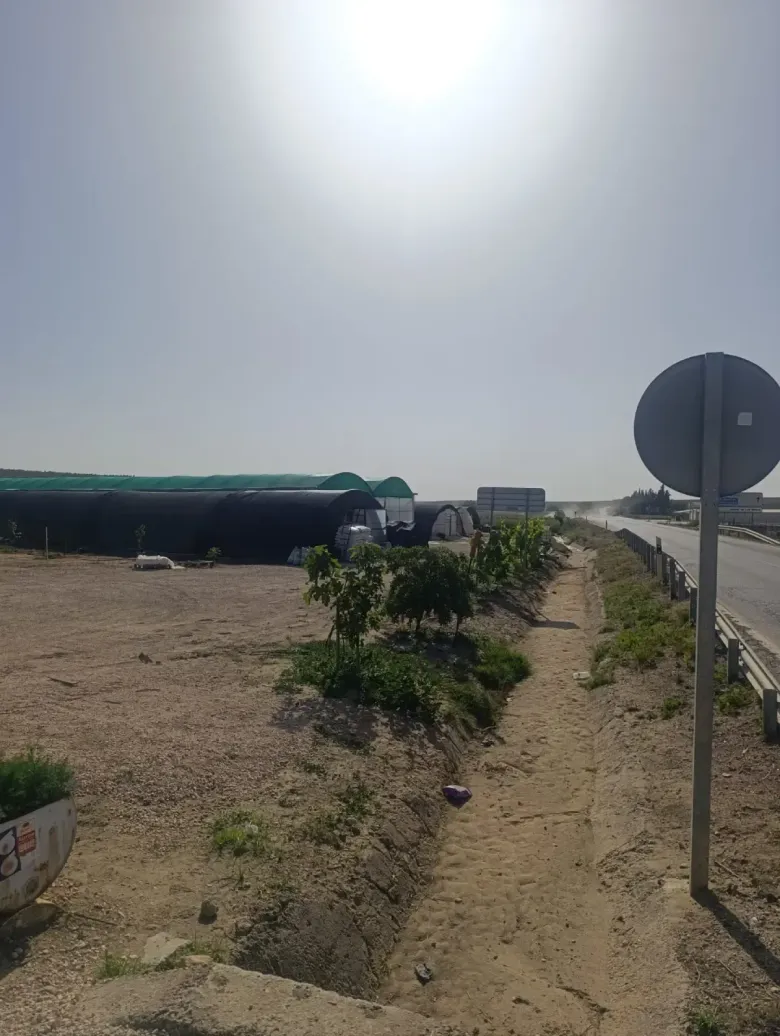 Borde polvoriento de la carretera con arbustos dispersos, una barrera de carretera y una señal de tráfico redonda