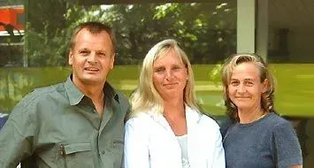 Drei Personen stehen im Freien Drei Personen stehen im Freien und lächeln vor einer grün getönten Glaswand.
