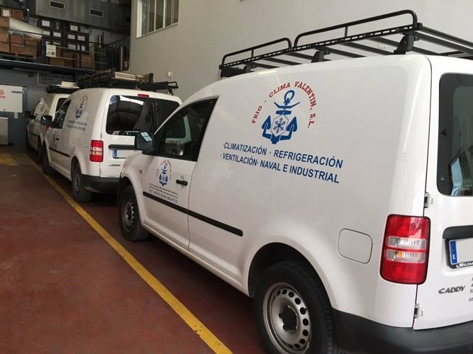 Furgonetas blancas con el logotipo de la empresa estacionadas dentro de un edificio. Las furgonetas tienen portaequipajes.