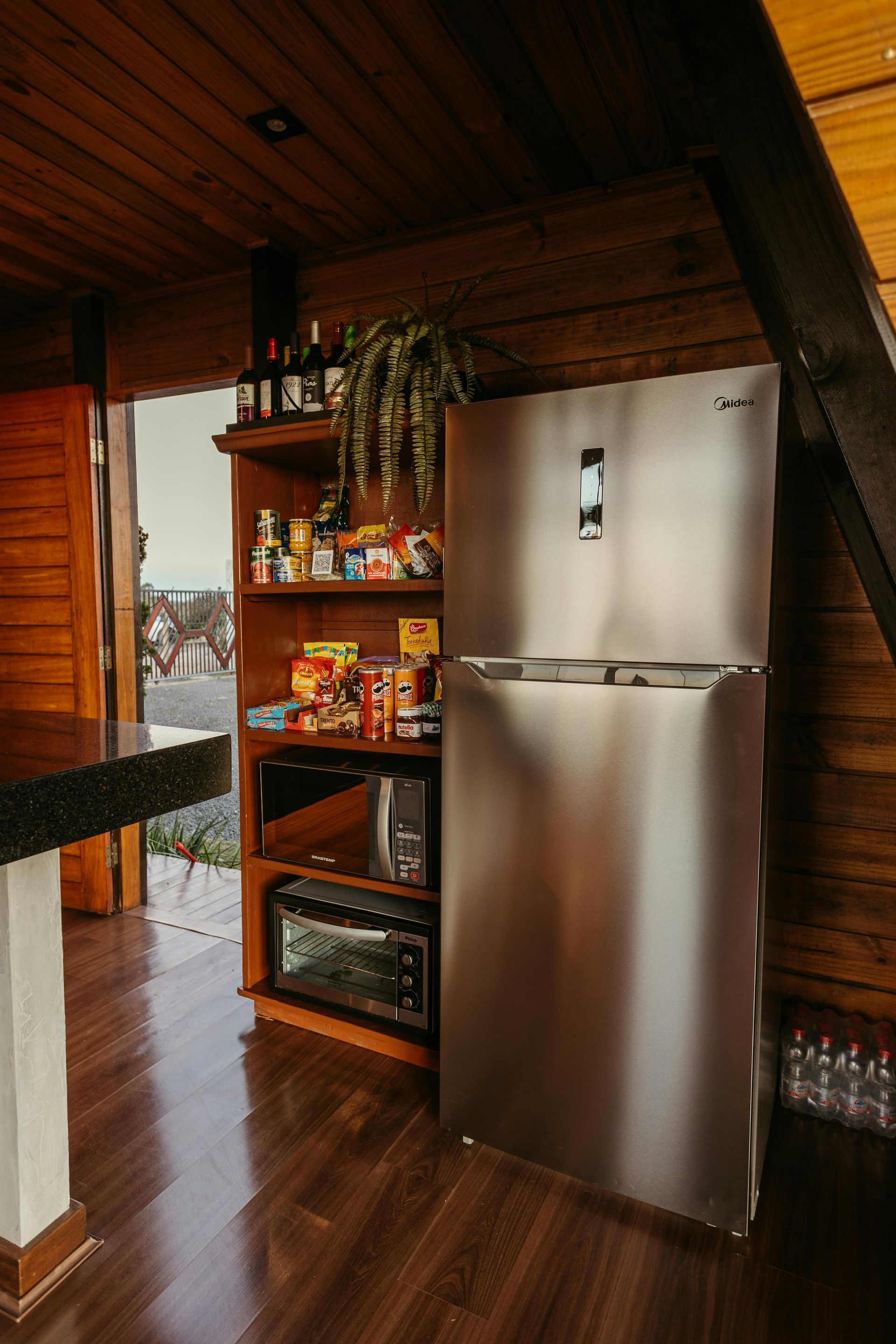 Ruostumattomasta teräksestä valmistettu jääkaappi ja ruokakomero mikroaaltouunilla mökin keittiössä. Puulattiat ja -seinät.