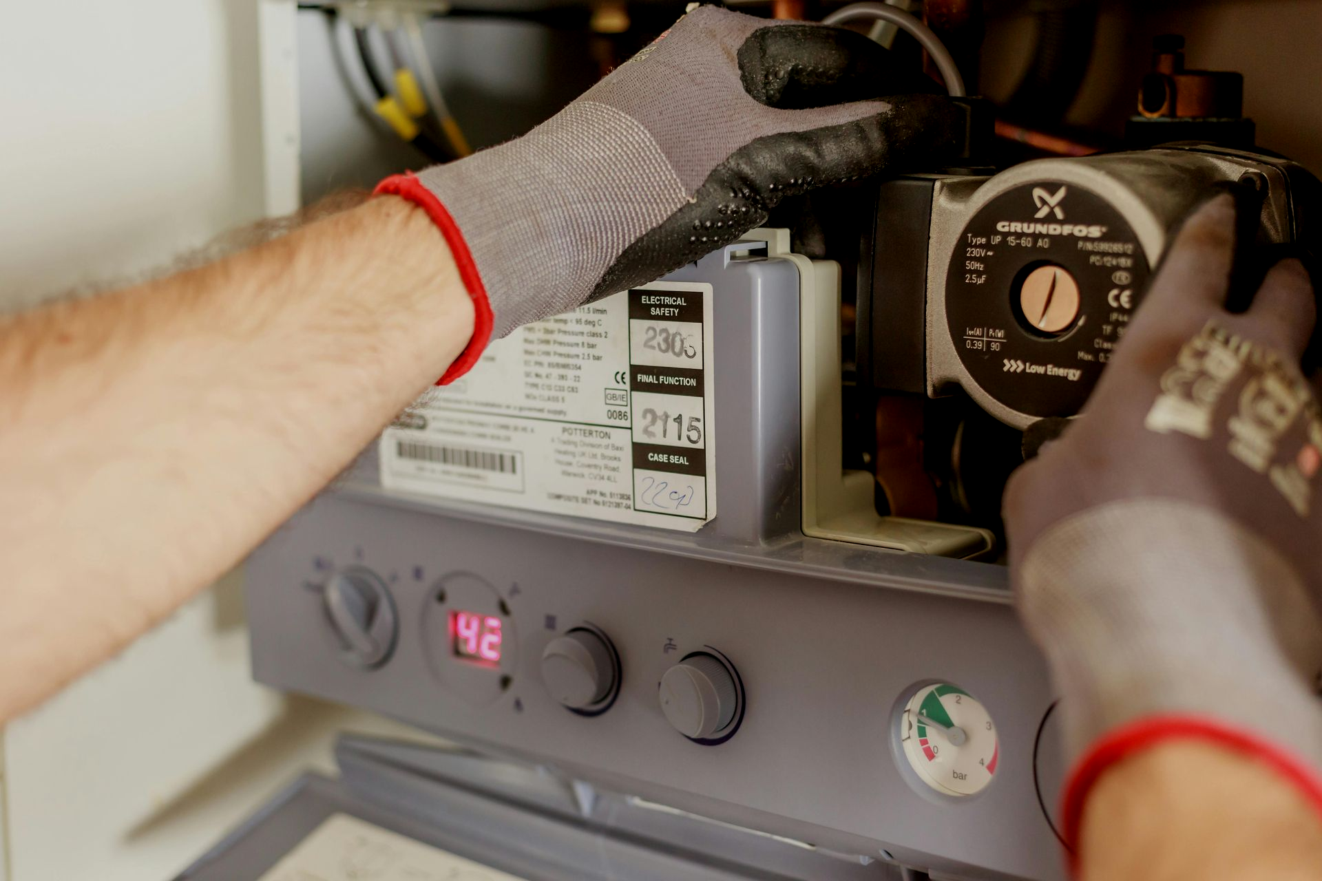 Henkilö käsineet päässä työskentelee kattilan parissa ja säätää pyöreää pumppua.