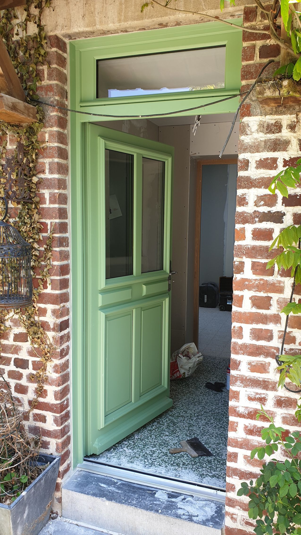 Porte verte, encadrée de briques, avec des vignes sur le côté.