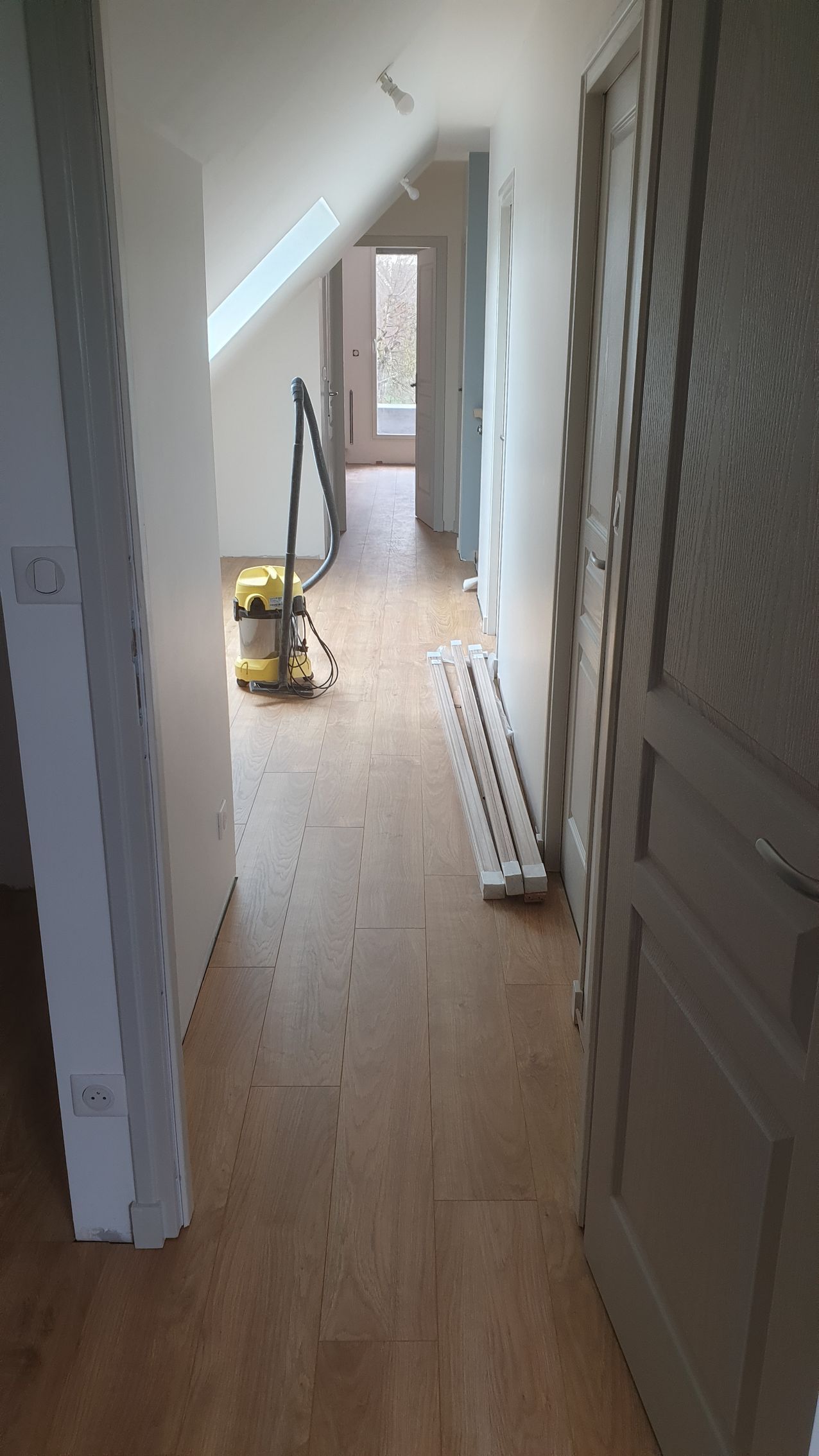 Couloir en bois avec parquet et portes marron clair.