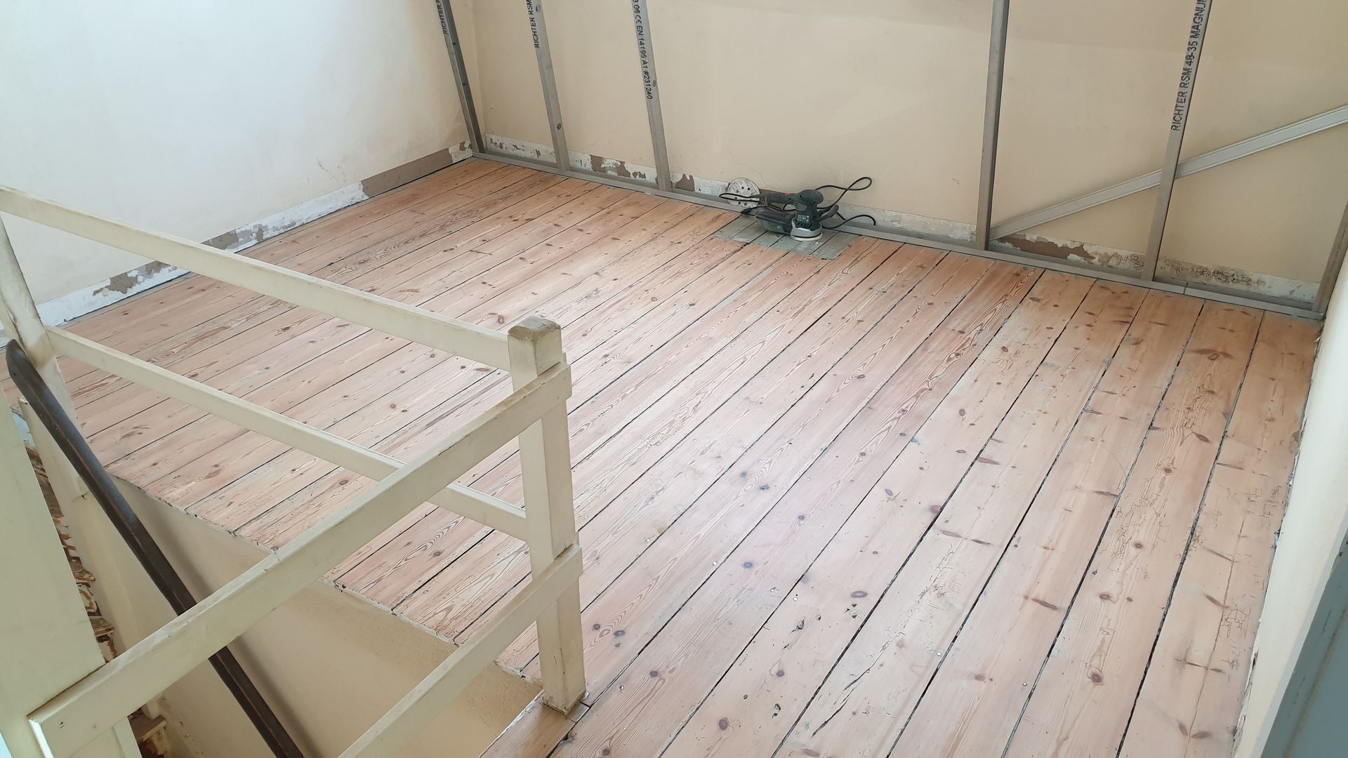 Vue aérienne d'une pièce avec parquet, escalier et murs couleur crème.