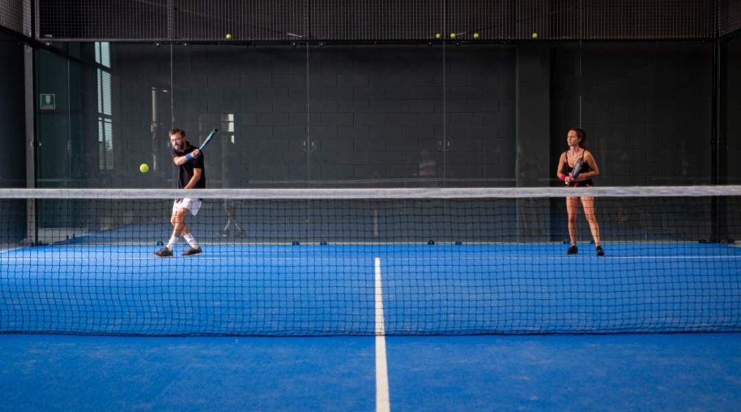 Un hombre y una mujer están jugando al pádel en una cancha azul.