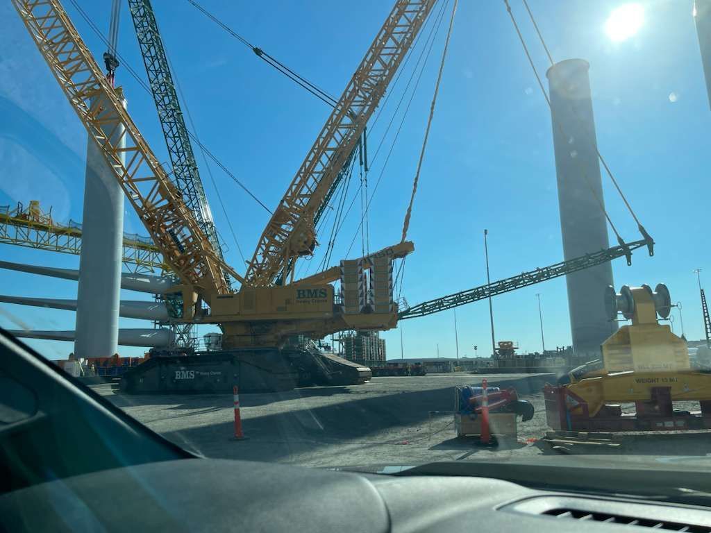 Large yellow crane at a wind turbine construction site on a sunny day.