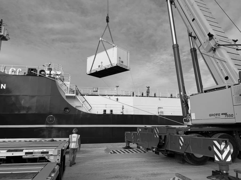 Cargo containers being loaded by cranes onto a barge at a waterfront port