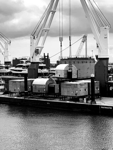 Cargo containers being loaded by cranes onto a barge at a waterfront port