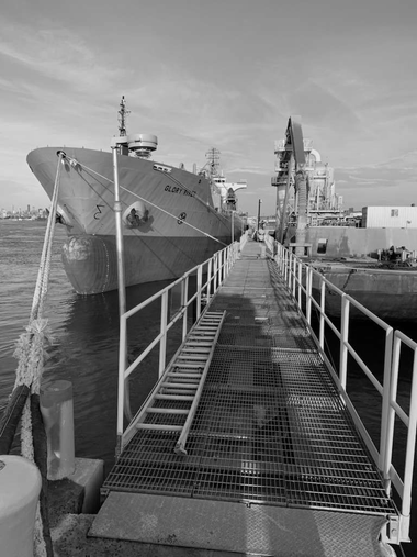 A warship moored beside a dock, with a metal gangway leading to its deck.