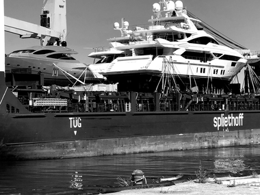Large yacht on a cargo ship at port, with reflections on the water.