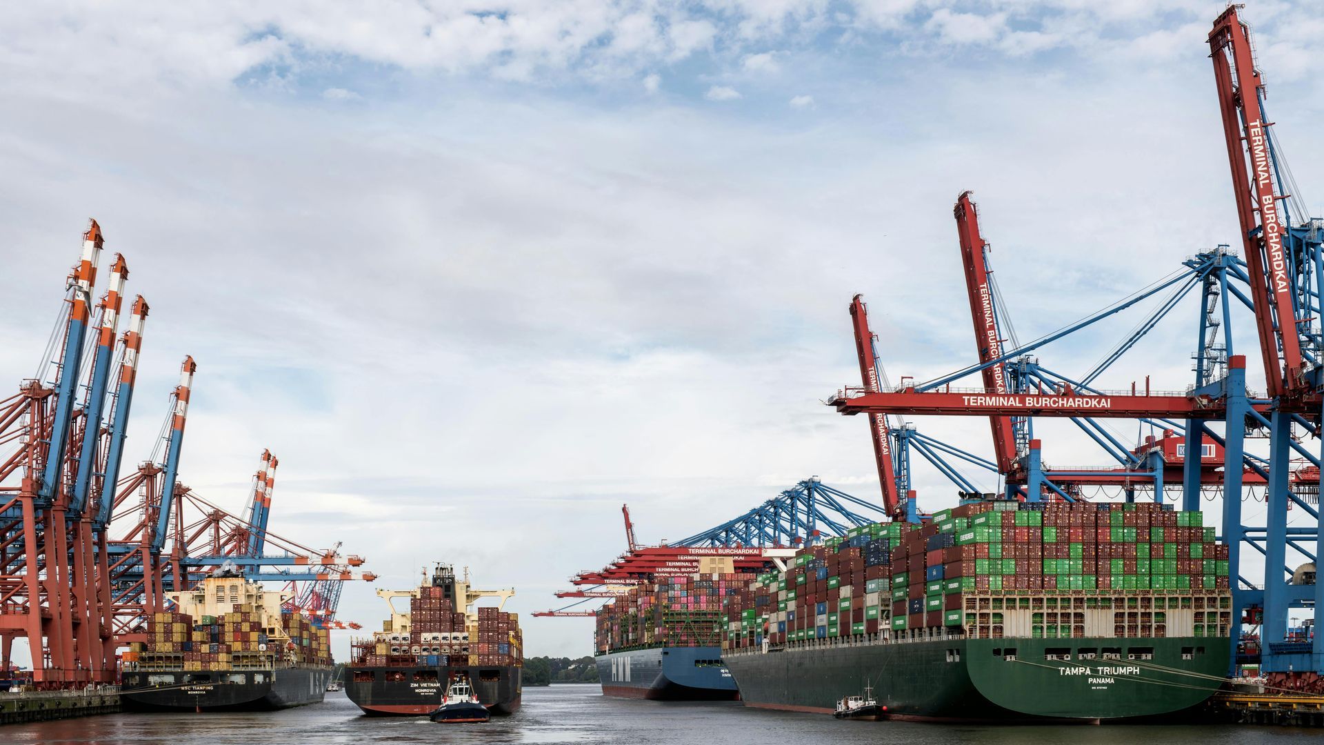 Two large yachts on a blue cargo ship. Cranes and support cables secure the yachts. Water and sky in background.