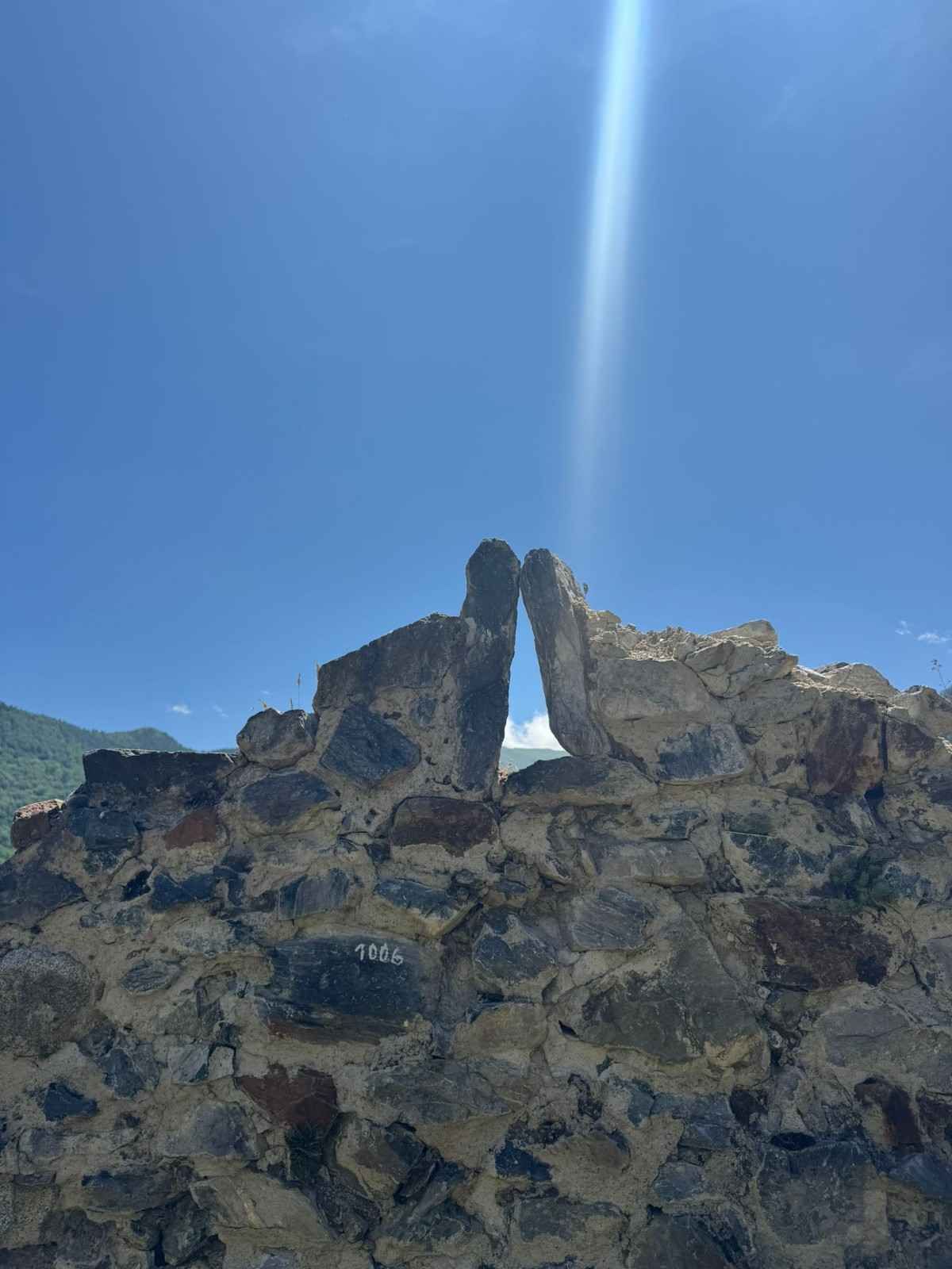 Pico de montaña rocosa bajo un cielo azul brillante con un rayo de sol que ilumina el centro.