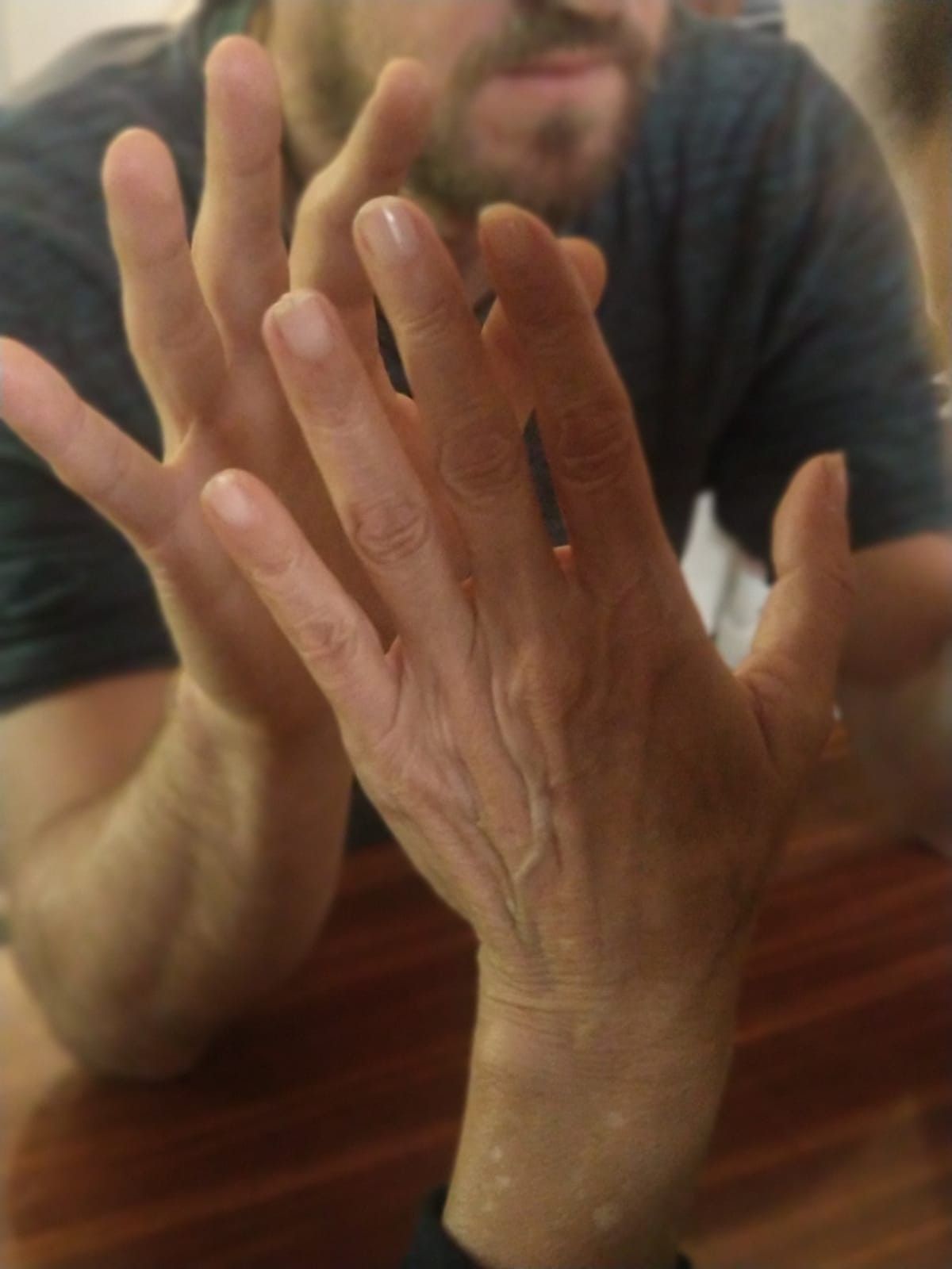 Dos manos alzadas frente a una persona sentada a una mesa, con el fondo borroso.