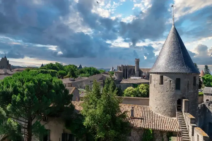 Un castillo de piedra se alza imponente sobre árboles verdes bajo un cielo parcialmente nublado.