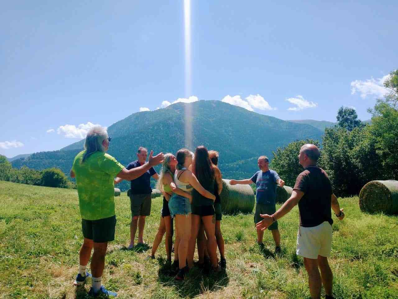 Personas de pie en un campo con los brazos en alto, montañas y un brillante rayo de sol al fondo.