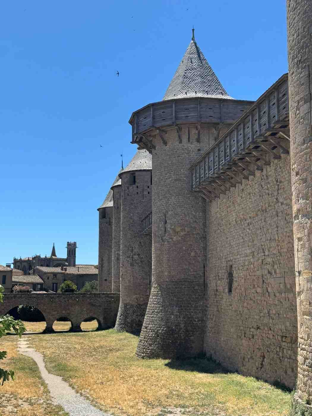 Puente de piedra sobre un río junto a un pueblo ribereño y un castillo bajo un cielo nublado.
