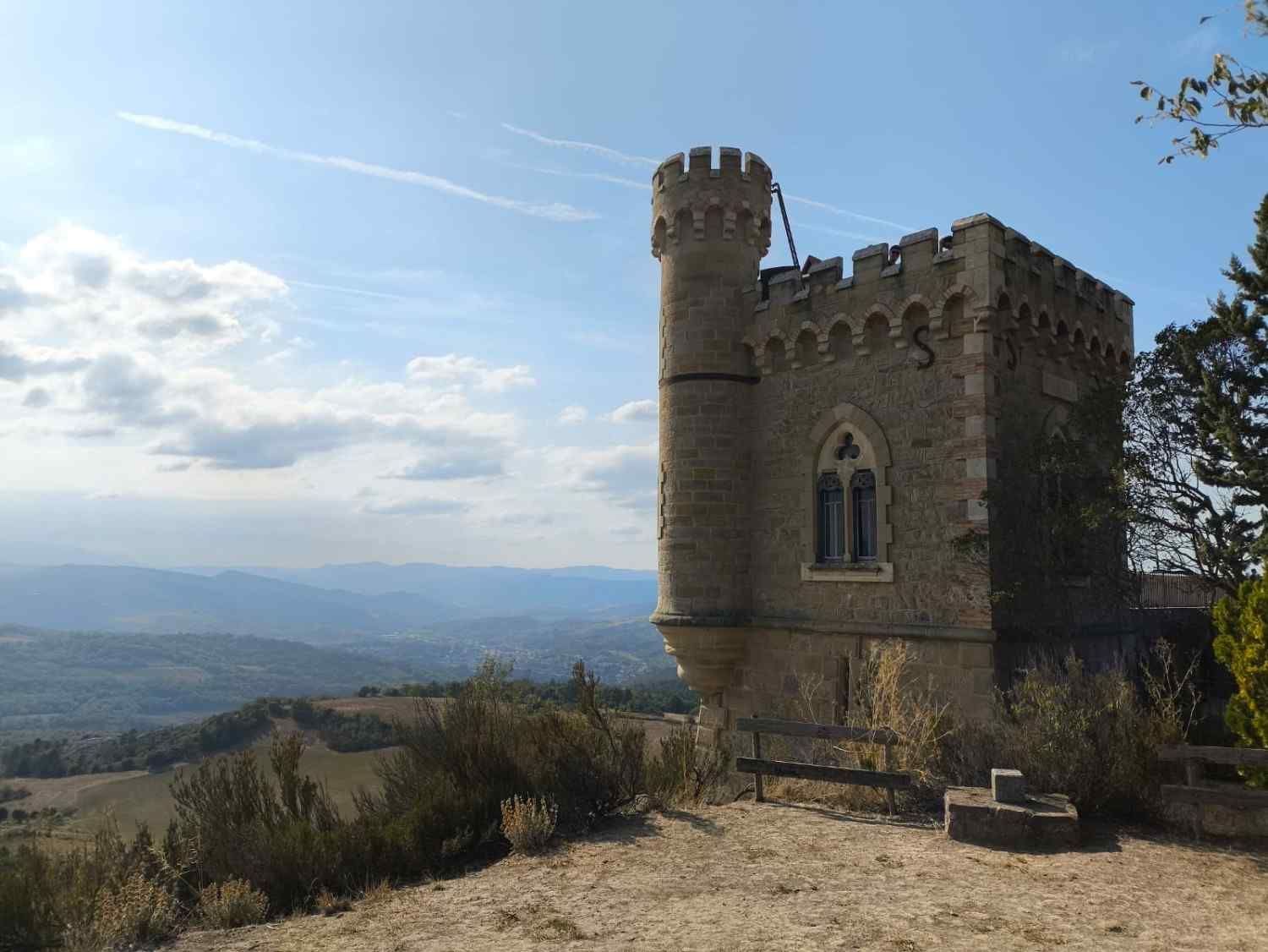 Torre de piedra en la cima de una colina con vistas a un valle lejano bajo un cielo azul.