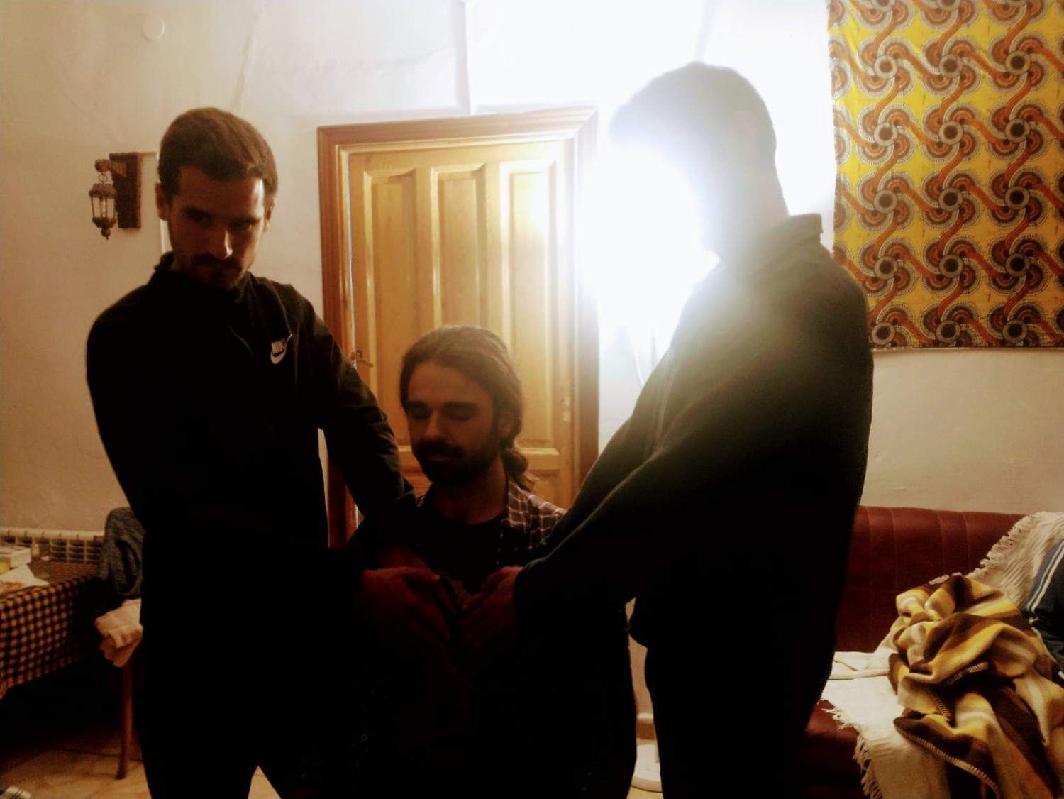 Tres personas están de pie alrededor de una persona sentada en una habitación con poca luz.