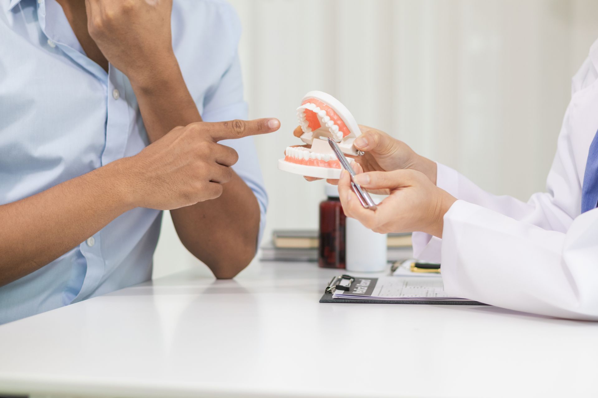 Ein Mann sitzt an einem Tisch und unterhält sich mit einem Zahnarzt, der ein Zahnmodell in der Hand hält