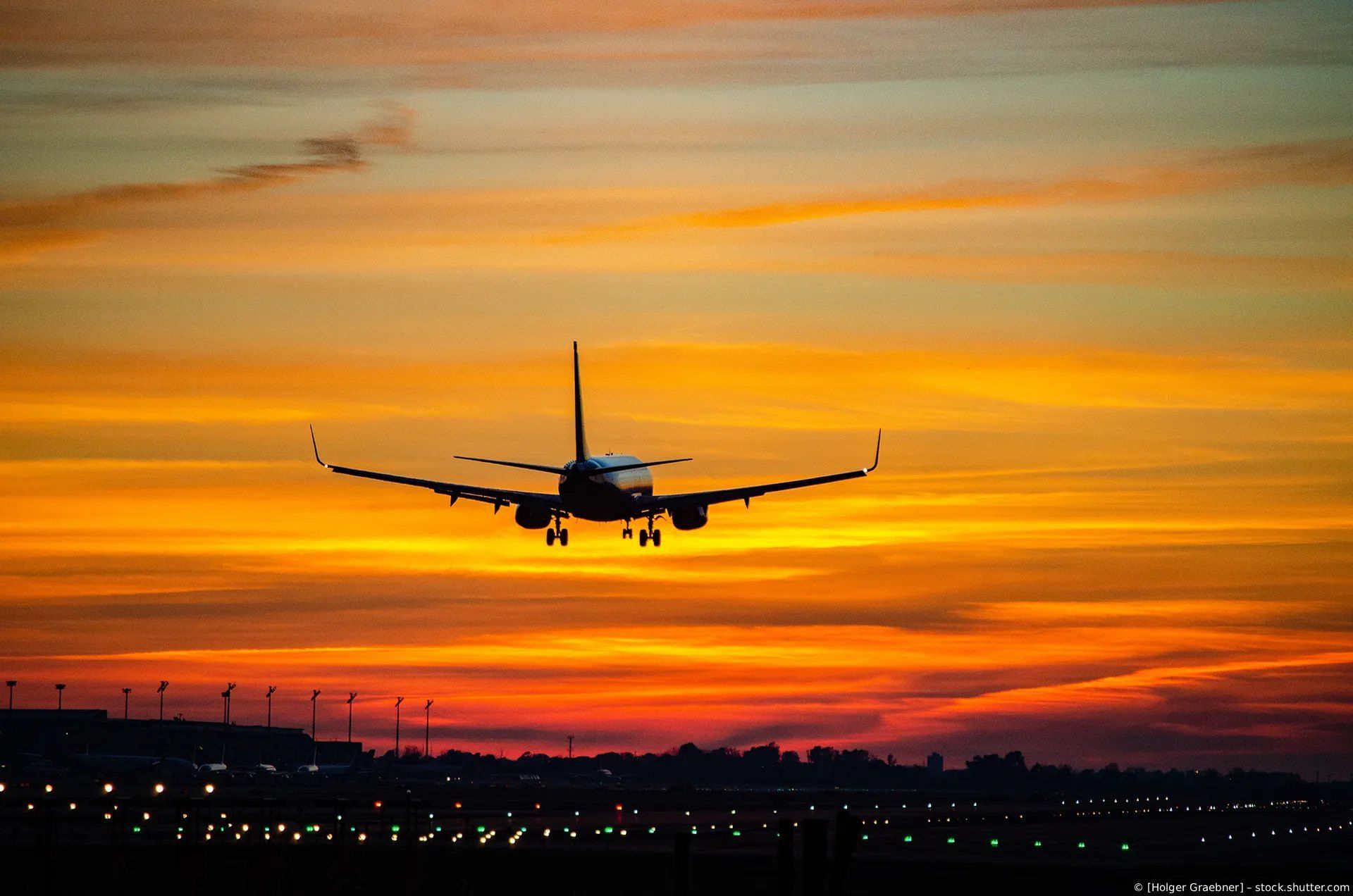 Flugzeug sinkt vor einem leuchtend orangefarbenen Sonnenuntergang über der Skyline einer Stadt