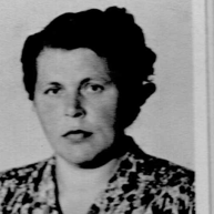 Schwarz-Weiß-Porträt einer Person mit kurzen dunklen Haaren und einer gemusterten Bluse, die in die Kamera blickt.