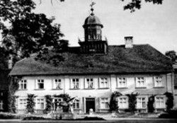 Schwarz-Weiß-Fotografie eines historischen zweistöckigen Gebäudes mit einem zentralen Turm und Bogenfenstern.