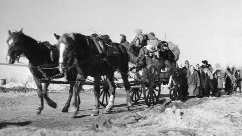 Eine Reihe von Menschen zieht von Pferden gezogene Schlitten durch eine verschneite Landschaft