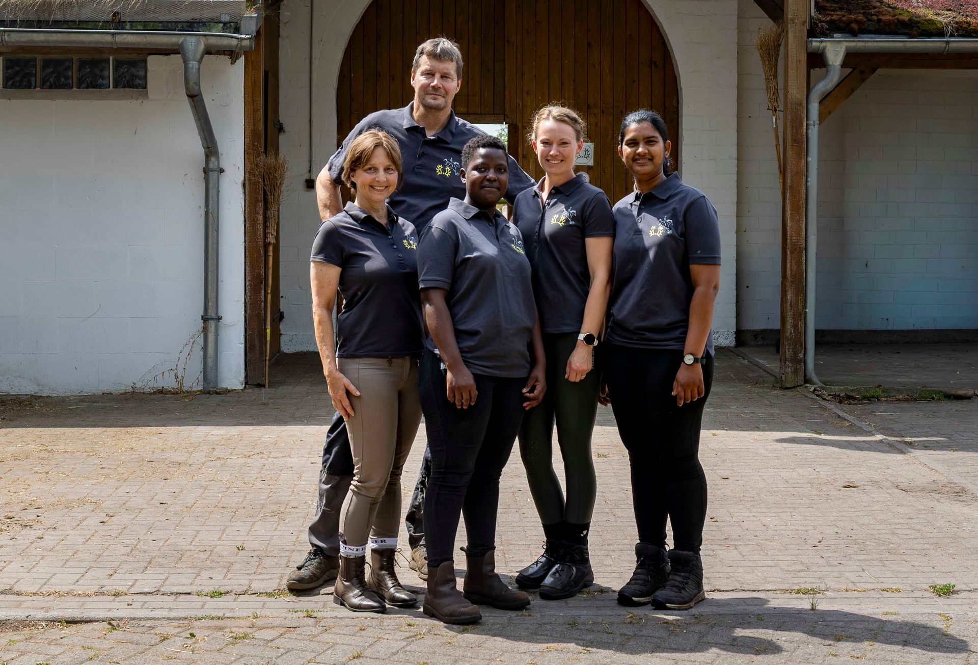 Fünf Personen in dunklen Uniformen stehen im Freien vor einem Gebäude zusammen.