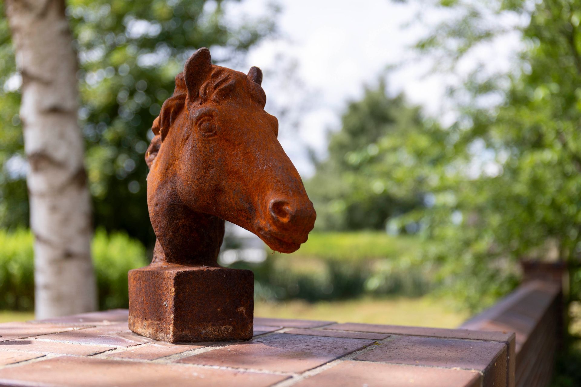 Rostfarbene Pferdekopffigur auf einem Holztisch im Freien, vor verschwommenem grünem Hintergrund.