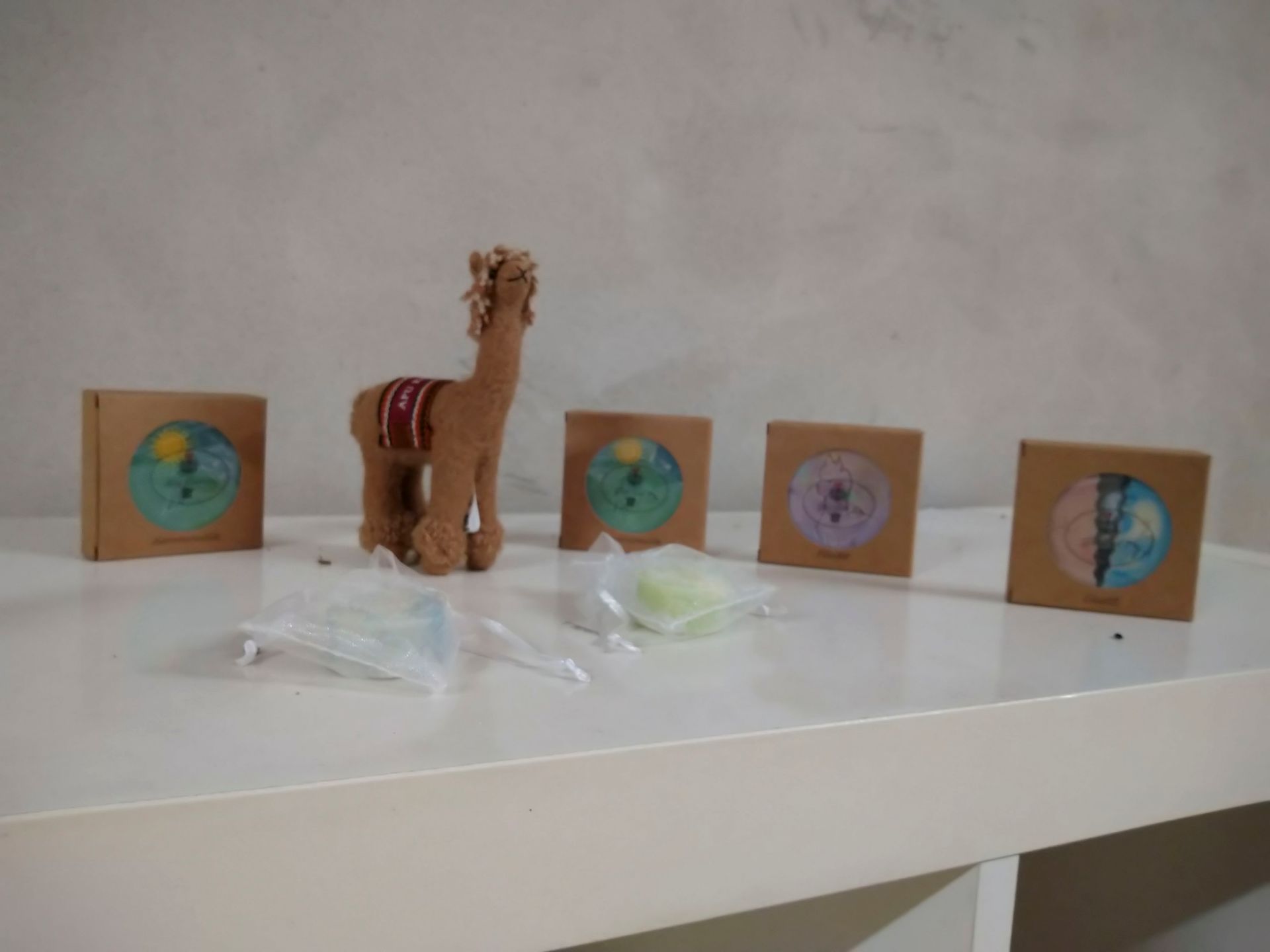 Eine kleine Lamafigur mit gestreifter Decke steht neben fünf bunten Kartenständern auf einem weißen Regal.