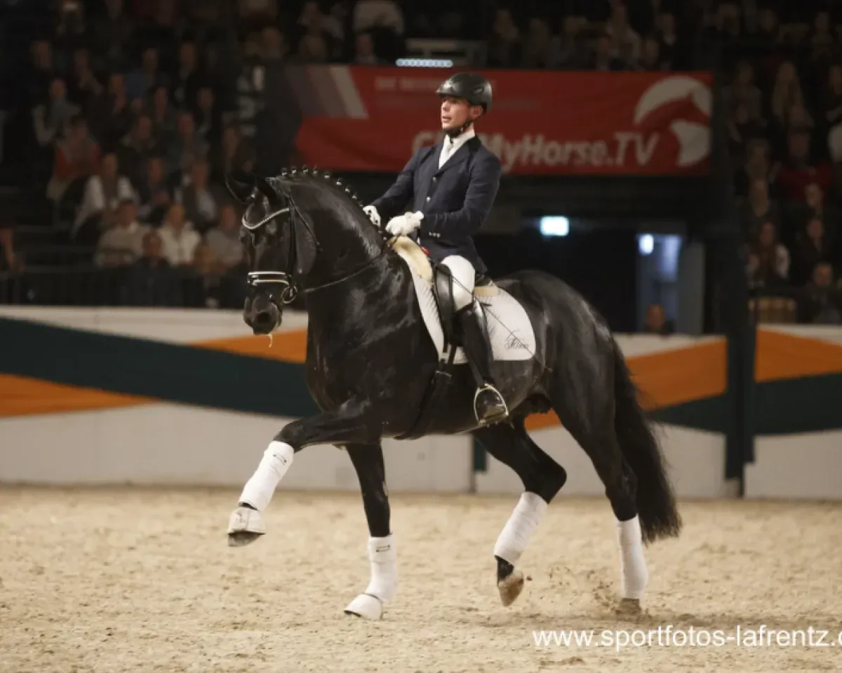 Schwarzes Pferd und Reiter in festlicher Kleidung führen eine Dressurprüfung in der Halle vor