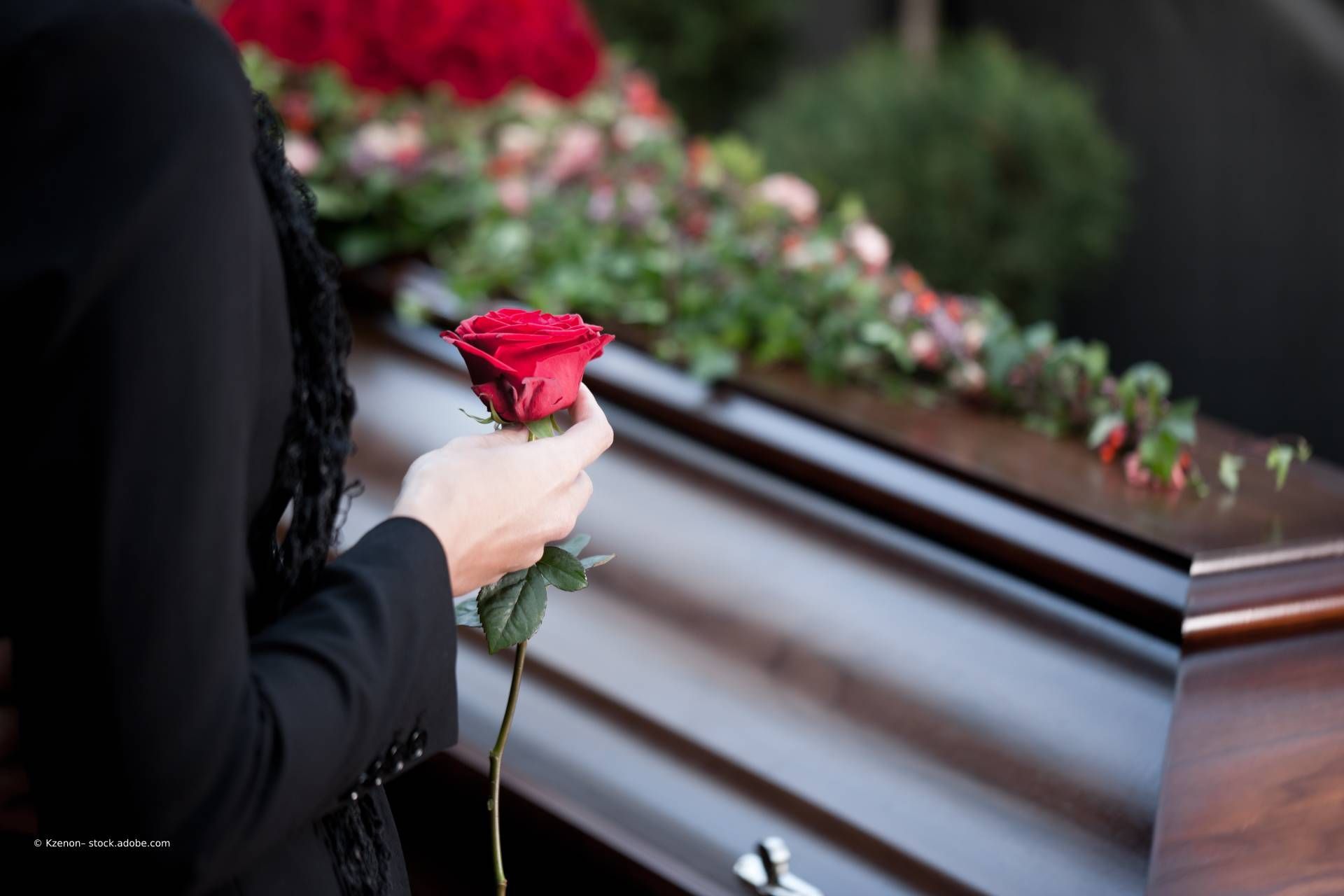 Frau steht mit einer Rose in der Hand an einem Sarg