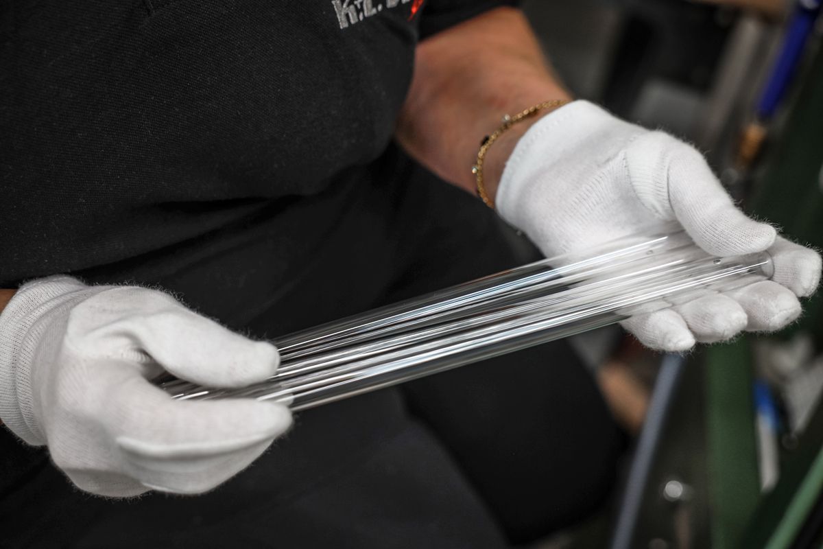 Eine Person mit weißen Handschuhen hält mehrere lange, durchsichtige, geriffelte Glasröhren.