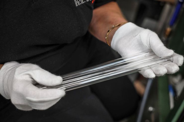 Eine Person mit weißen Handschuhen hält mehrere lange, durchsichtige, geriffelte Glasröhren.