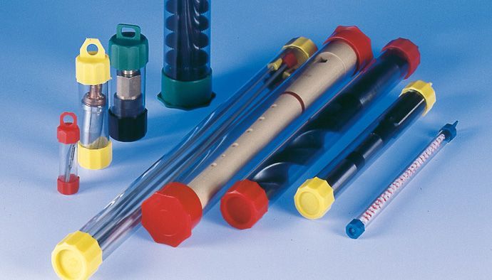 Sammlung durchsichtiger, zylindrischer Röhrchen mit farbigen Kappen, einige davon mit Messgeräten, vor blauem Hintergrund.