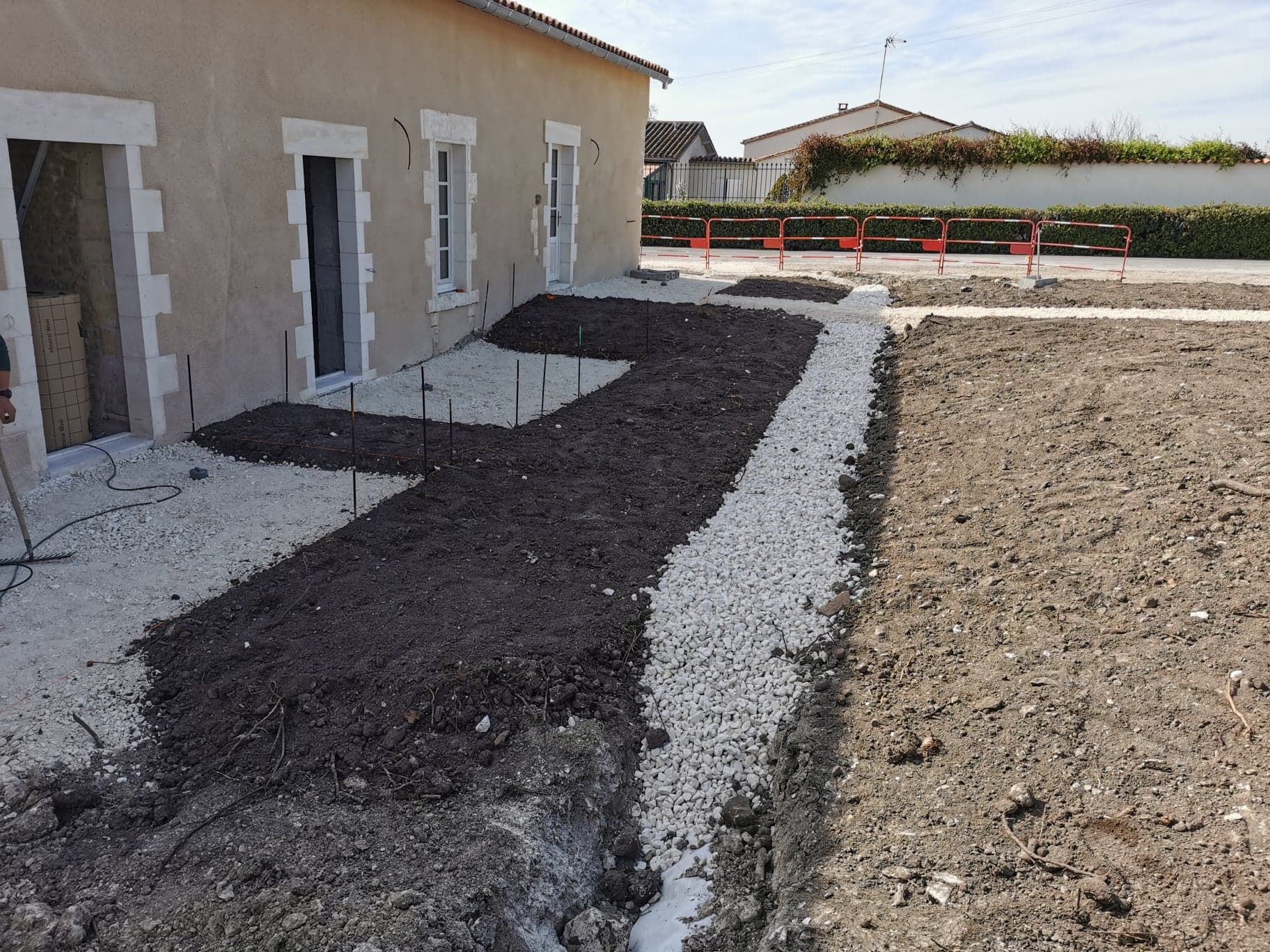 Cour nouvellement aménagée à côté d'une maison en stuc, avec des allées de gravier et un sol nu en cours de construction.