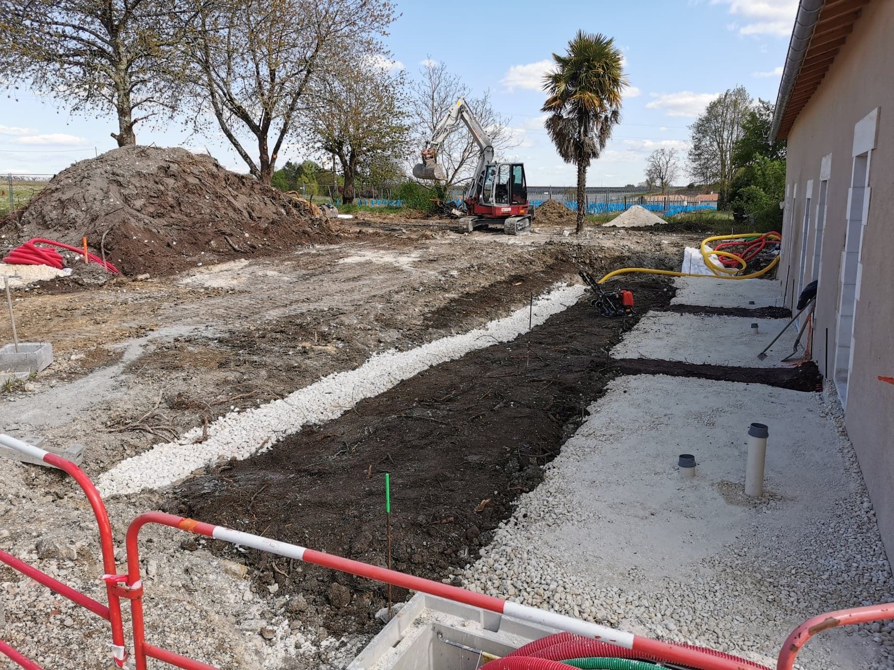 Tranchée de construction à côté d'une maison avec du gravier, des tas de terre et une petite excavatrice
