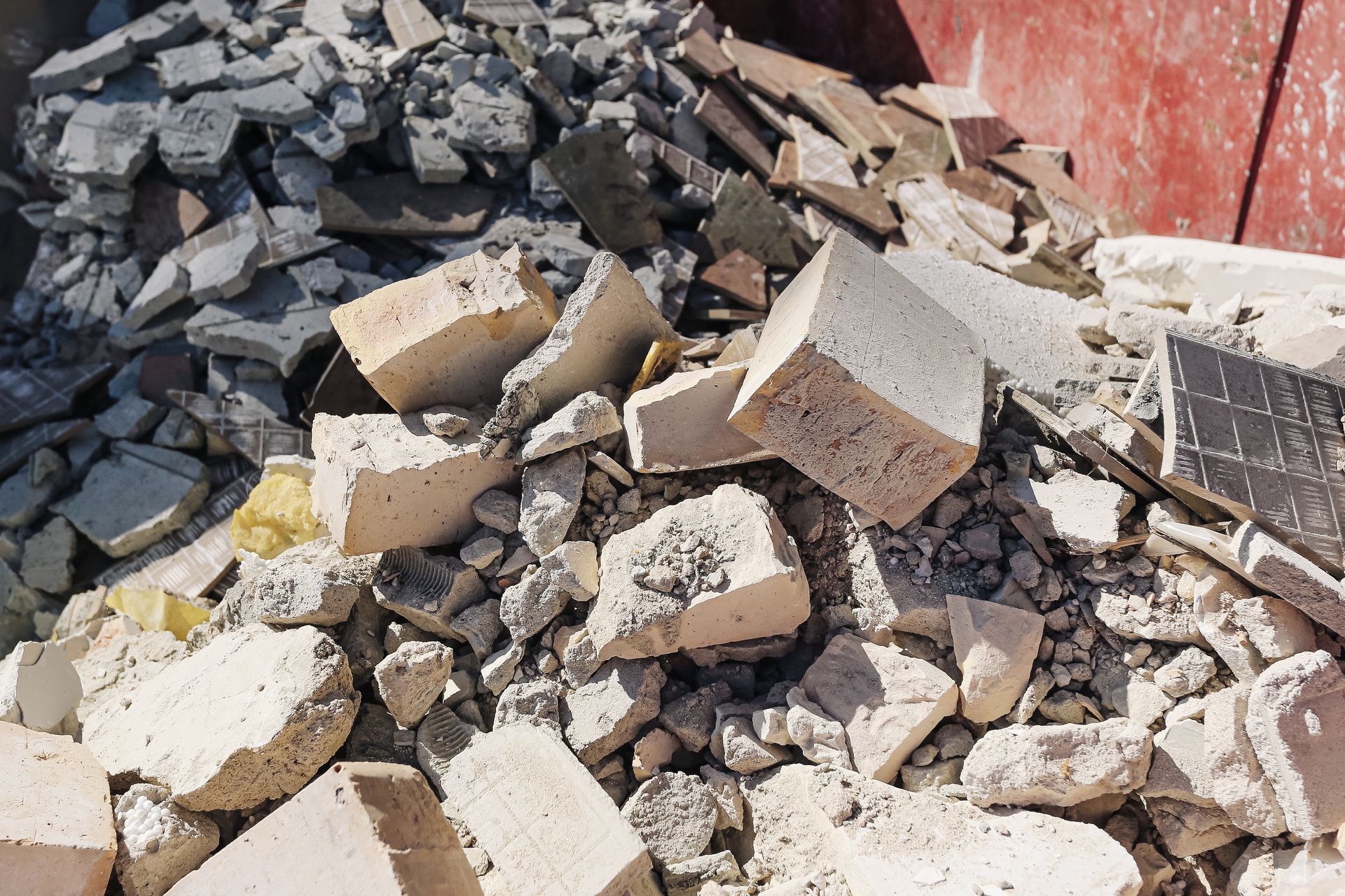 Tas de béton cassé et de gravats mêlés à des parpaings près d'un mur rouge