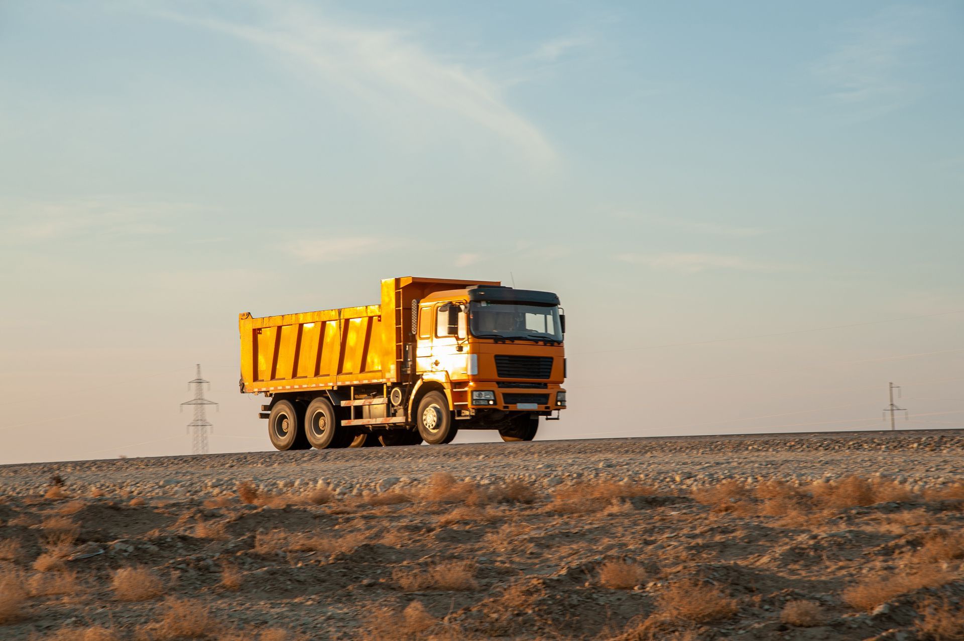 Un camion-benne jaune roule sur un chemin de terre sous un ciel dégagé