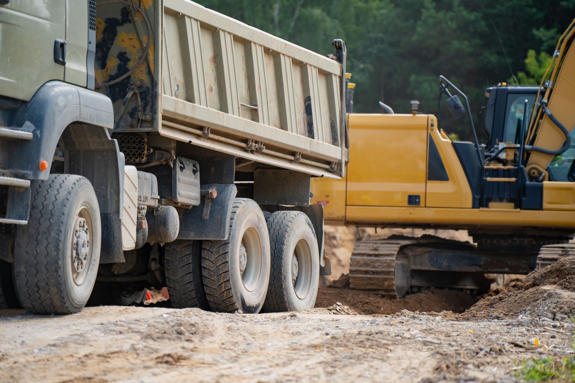 Des camions de chantier sur un chemin de terre, une pelleteuse jaune creusant à côté d'un camion-benne.