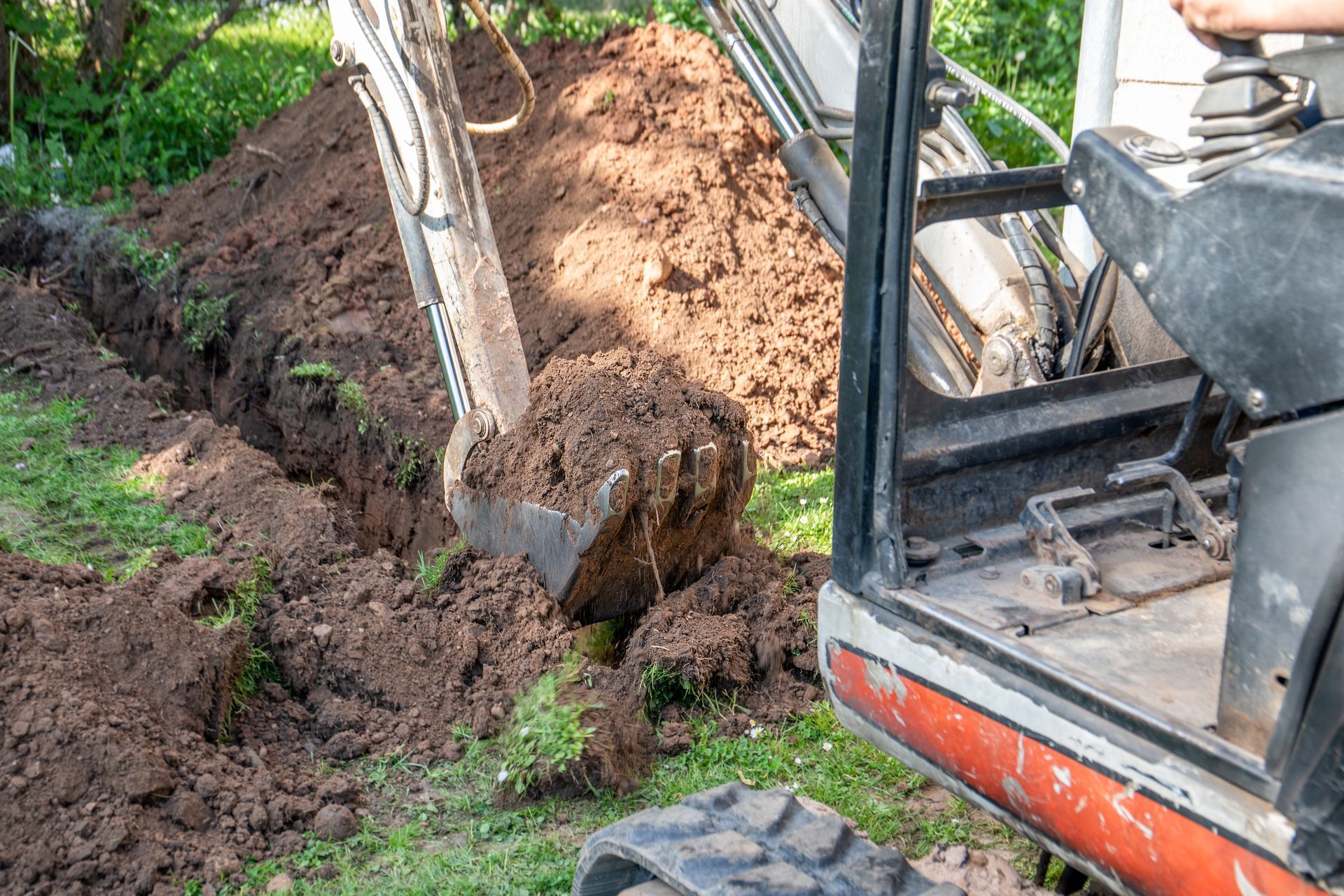 Une excavatrice creuse une tranchée à côté d'un tas de terre sur un chantier de construction boisé.