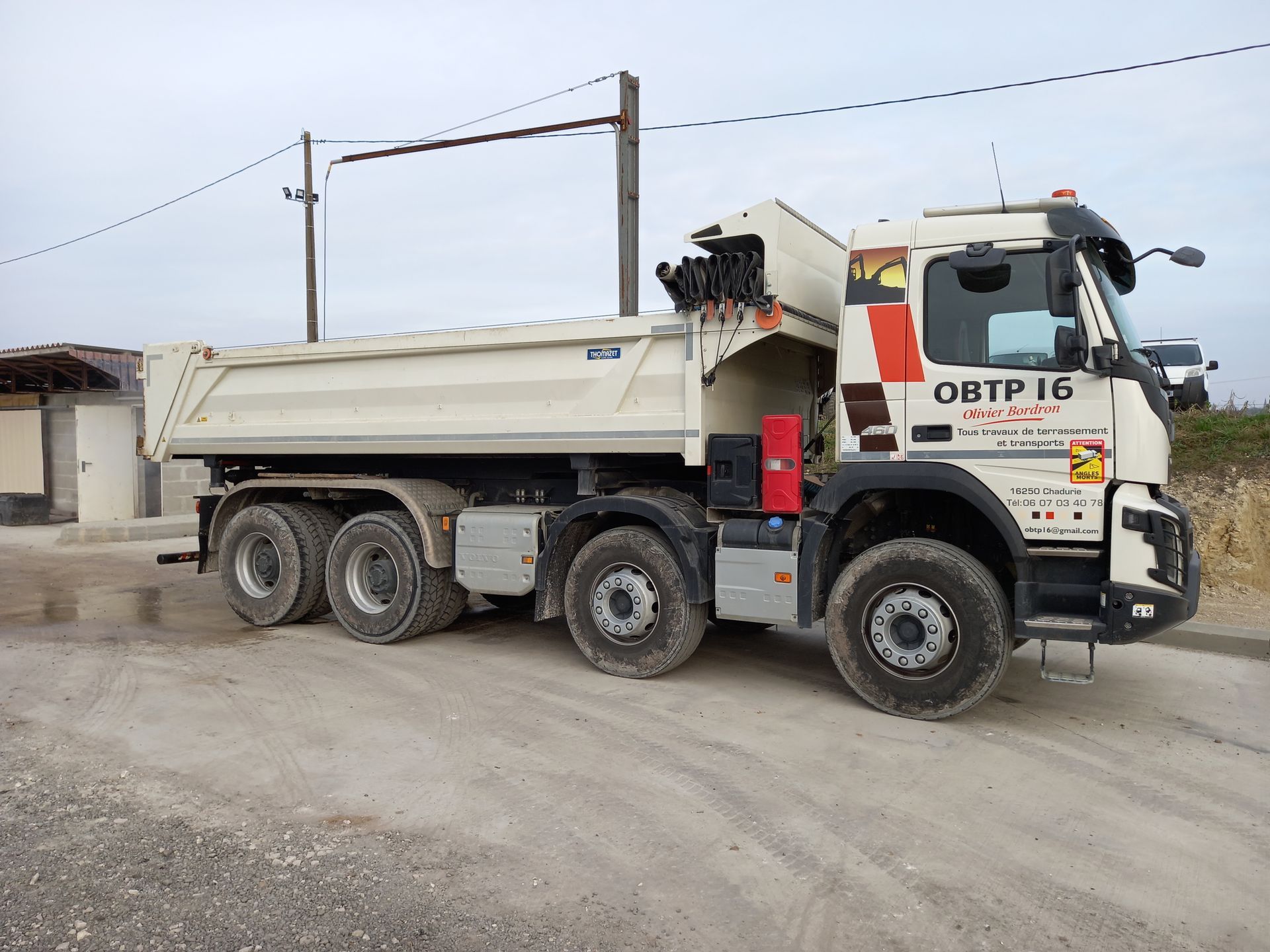 Camion-benne blanc stationné sur un terrain gravillonné, vu de côté.