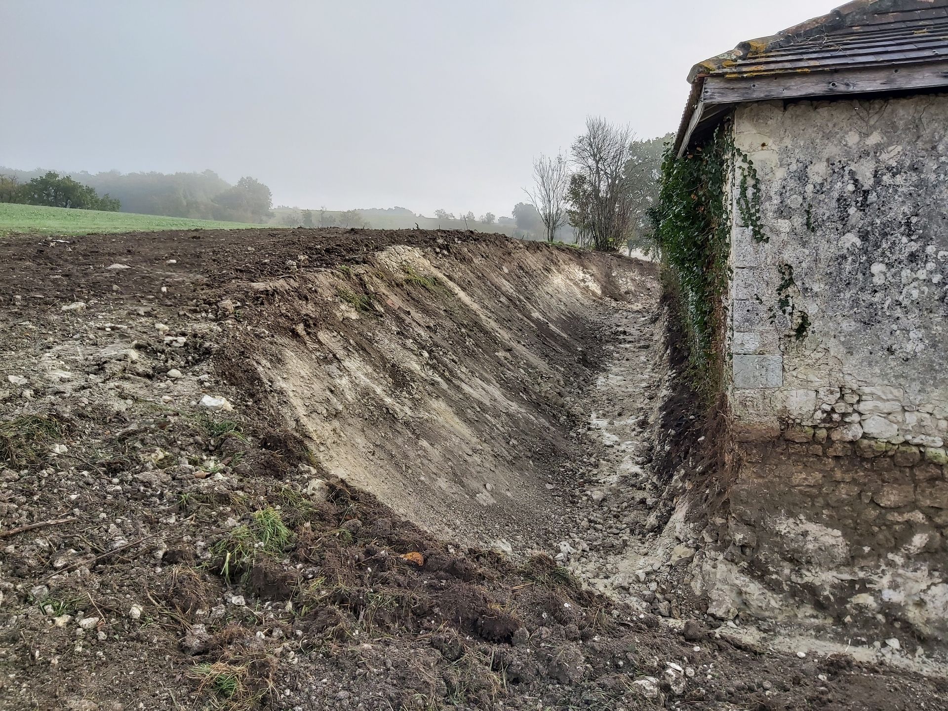 Un talus de terre effondré jouxte un mur délabré dans un champ boueux.