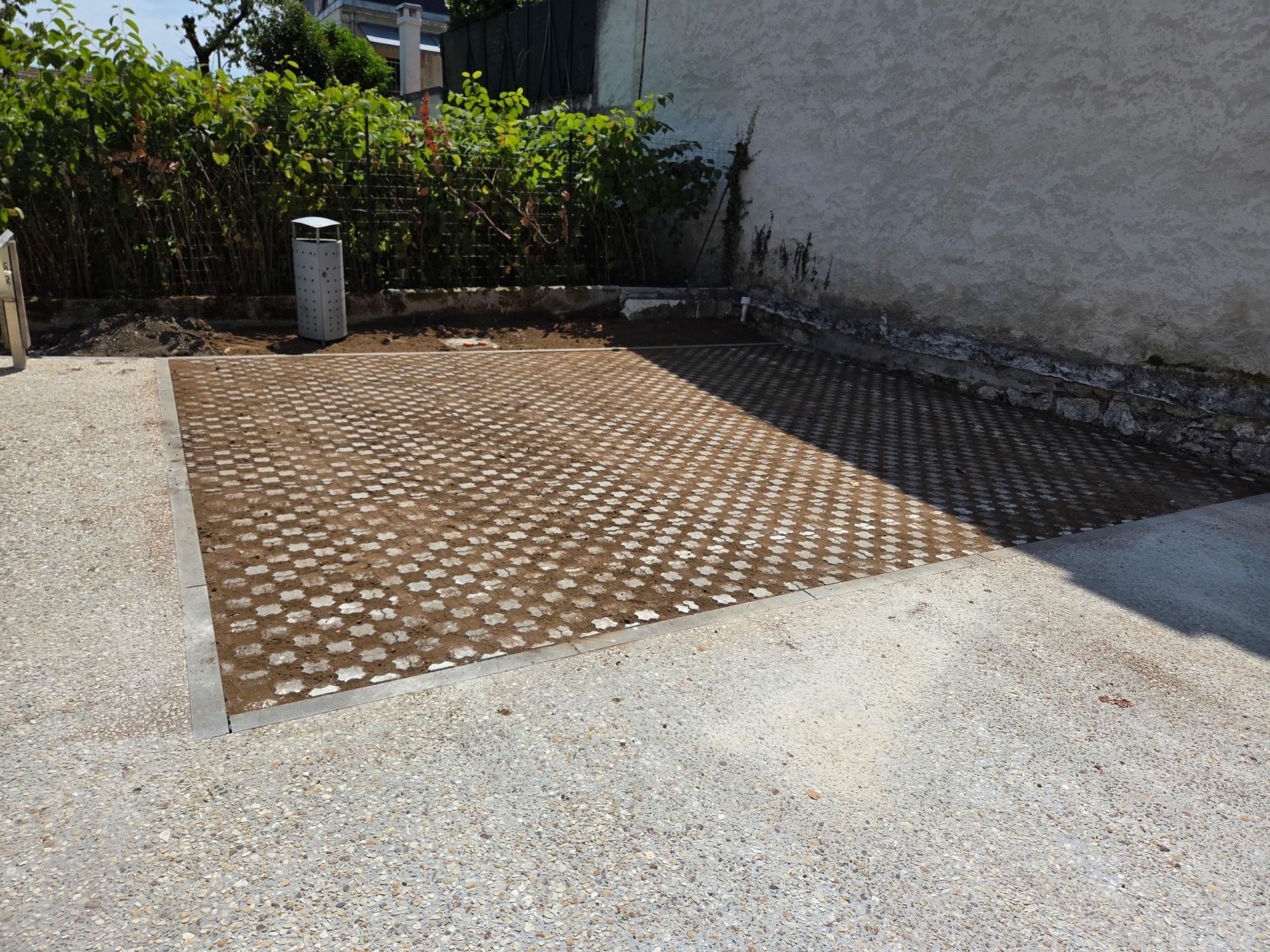 Sol pavé longeant un mur, avec une surface beige à motif quadrillé et un premier plan en gravier.