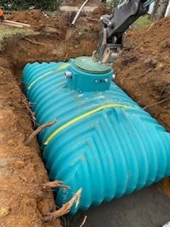 Réservoir souterrain à nervures bleues installé dans une tranchée de terre par un bras d'excavatrice