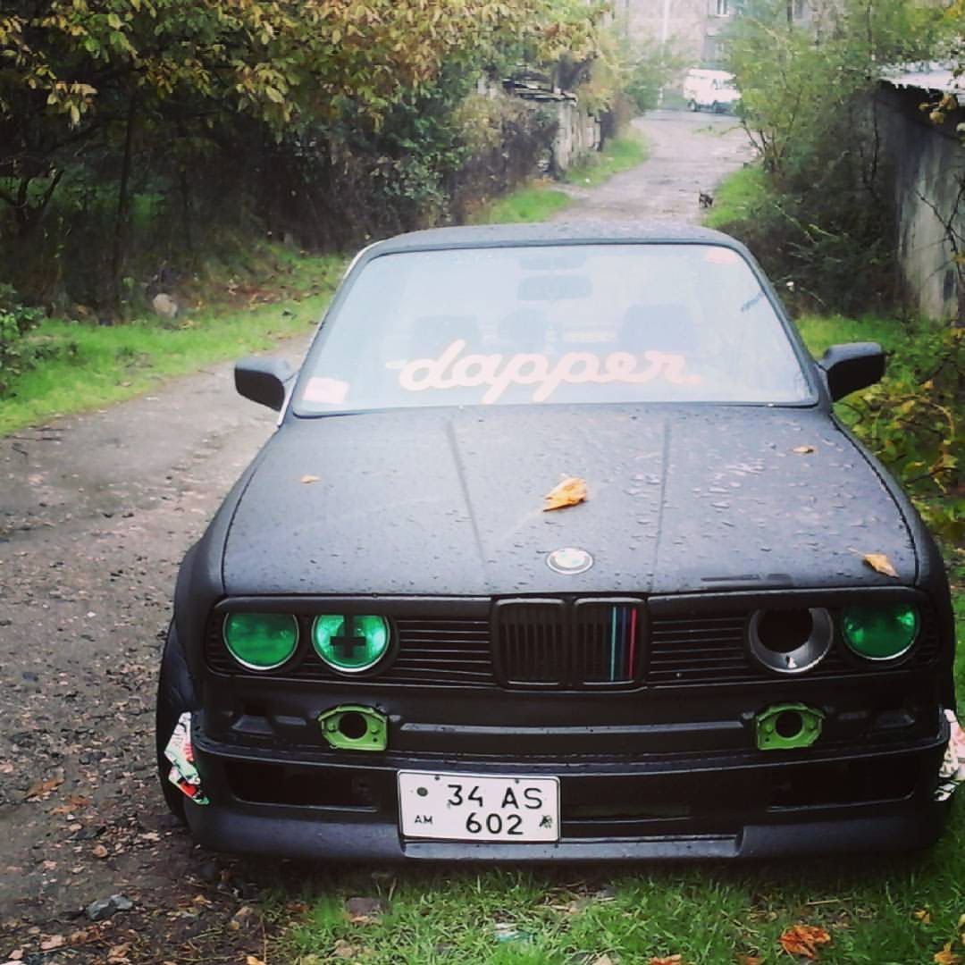 Voiture BMW noire avec des accents verts garée sur un chemin étroit et herbeux ; « pimpante » sur le pare-brise.